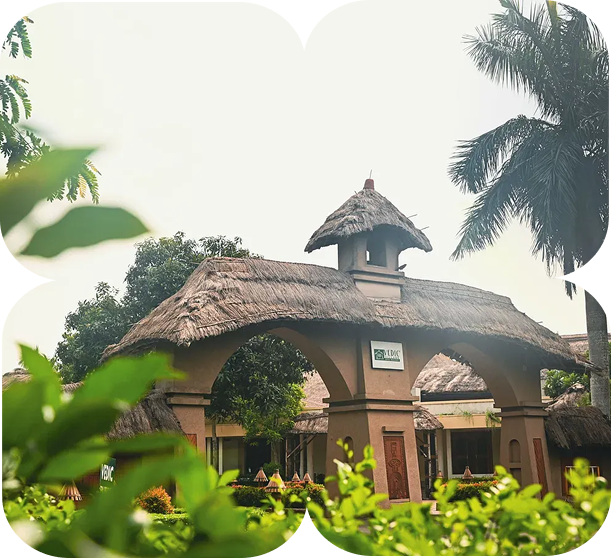 Entrance of Vedic Village with thatched roof gate surrounded by greenery